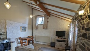 A cozy attic room with exposed wooden beams, a stone wall, a sofa, a dining table, and a television. - Elegant and Secluded 1-bed Cottage Near Bideford (Bideford)