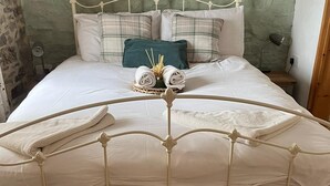 A neatly made bed with a metal frame, white bedding, and a green pillow. There is a small table with a lamp and a bottle of water next to the bed. - Elegant and Secluded 1-bed Cottage Near Bideford (Bideford)