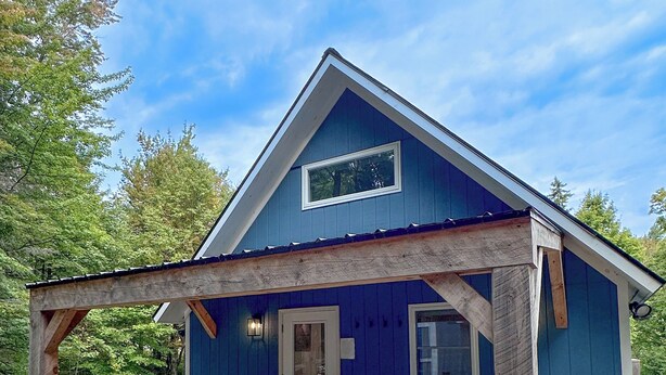 A blue cabin with a hot tub, two Adirondack chairs, and a covered patio area. - Brand New, Private Home w/ Nordic Hot Tub- Just 1/2 mile to Jay Peak Resort (Jay)
