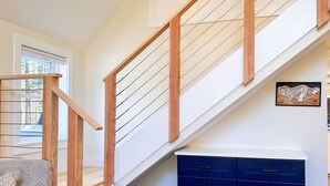 A modern staircase with wooden railings and a built-in bench, leading to a dark blue cabinet under a sloped ceiling. - Brand New, Private Home w/ Nordic Hot Tub- Just 1/2 mile to Jay Peak Resort (Jay)