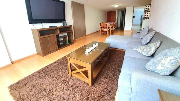 Un salon moderne avec un téléviseur à écran plat, un meuble de rangement en bois, un canapé agrémenté de coussins à motifs et, au fond, un coin repas.
