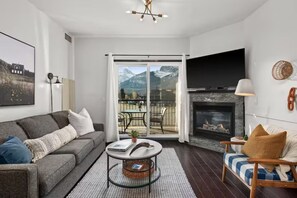 Una sala de estar con sofá, sillón, chimenea y vistas a montañas a través de un ventanal.