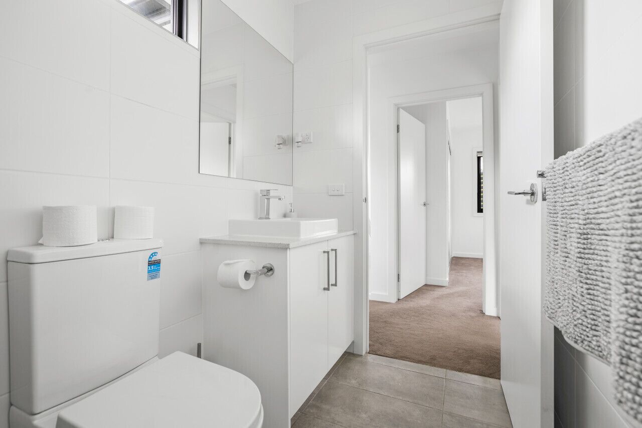 Une salle de bain moderne avec des éléments d’équipement blancs, des toilettes, un lavabo et un miroir.