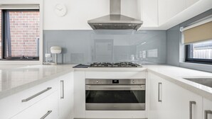 A modern kitchen with a stainless steel range hood, a built-in oven, and a large window with a view of a brick building. - StayAU Modern 4BRM TH Bayswater (Bayswater North)