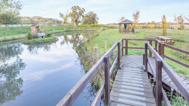 A wooden deck leading to a pond with a gazebo and picnic tables in the background.
