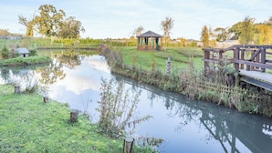 A serene outdoor setting with a wooden gazebo, a wooden bridge, and a calm pond reflecting the sky.