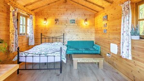 A wooden cabin room with a bed, a sofa, a bench, and a window with curtains.