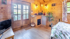 A wooden cabin interior with a TV, a bed, a kitchen area, and a large window.