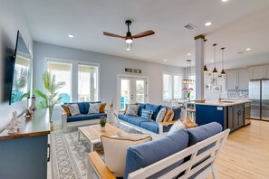 A modern living room with a sofa, coffee table, and a dining area. There is a kitchen with a refrigerator and cabinets. - Steps to Sand! Group-Friendly Getaway in Galveston (Galveston)