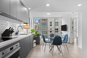 Une cuisine moderne avec des armoires grises, une cuisinière encastrée et un évier. On y trouve également un coin repas avec des chaises bleues et une table.