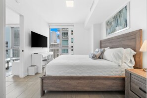 A modern bedroom with a large bed, a TV mounted on the wall, and a view of the cityscape through the window.