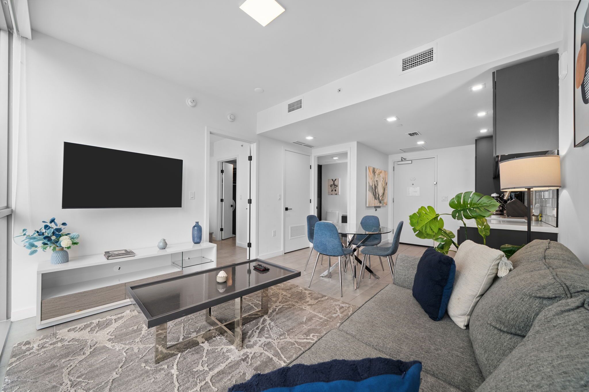 A modern living room with a flat-screen TV, a glass coffee table, and a grey sofa.