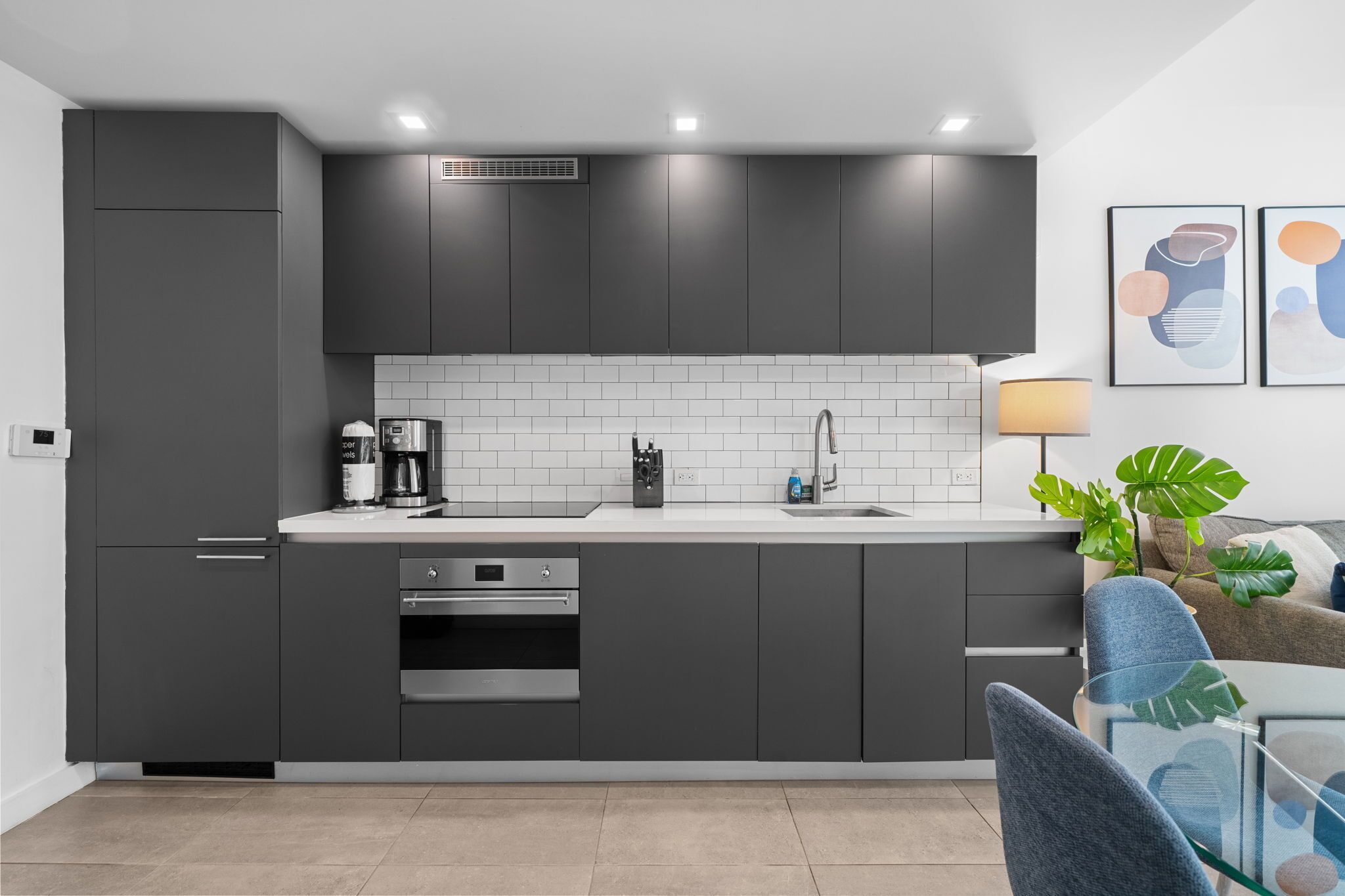 Uma cozinha moderna com armários cinza, painel de azulejos branco, forno embutido e cafeteira.