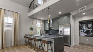 Una cocina moderna con una isla central, taburetes de bar, electrodomésticos de acero inoxidable e iluminación colgante.