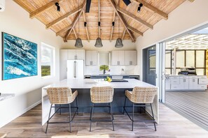 A modern kitchen with a large island, three wicker bar stools, and pendant lighting.