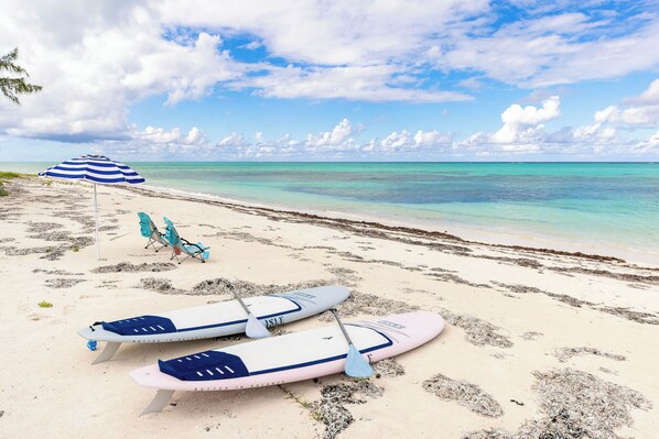 A beach with surfboards and a blue and white striped umbrella.