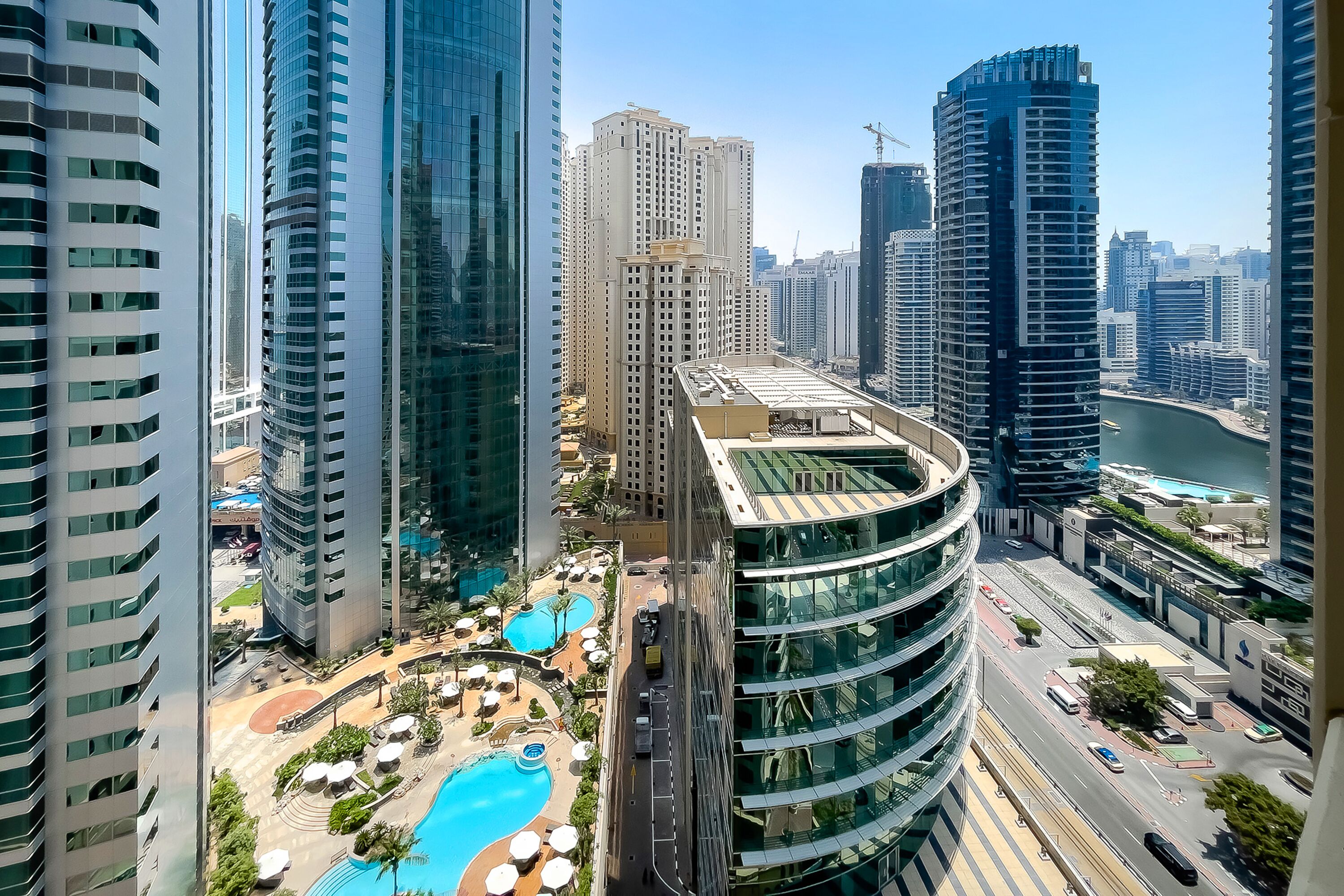 A high-rise hotel with a curved glass facade, a rooftop pool, and a view of a river and other buildings.