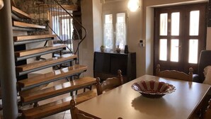 Eine Holztreppe führt zu einer zweiten Etage, einem Essbereich mit Tisch und Stühlen sowie einer Tür mit Fenstern.