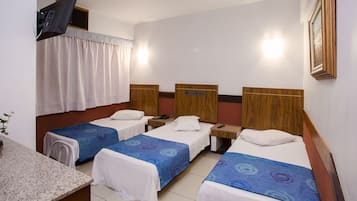 A hotel room with four single beds, a small desk, and a television mounted on the wall.
