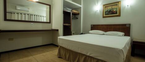 Quarto de hotel com uma cama grande, um guarda-roupa, um espelho e um quadro na parede.