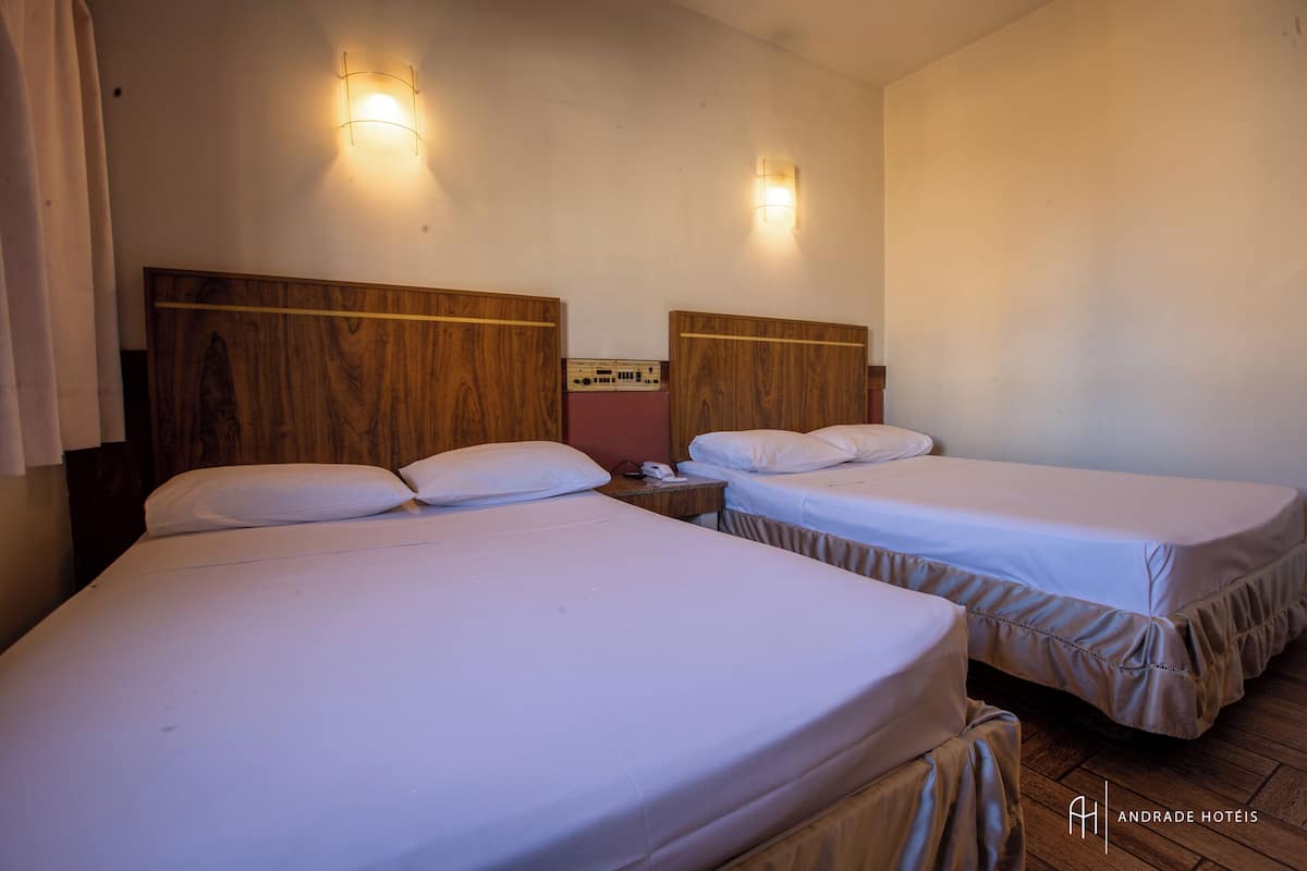 A hotel room with two single beds, wooden headboards, bedside tables, and wall-mounted light fixtures.