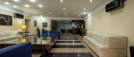 A modern hotel lobby with a checkered floor, a blue sofa, a white sofa, and a glass coffee table.