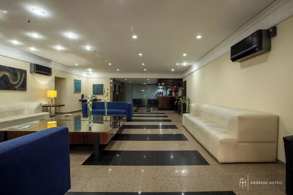 Un moderno vestíbulo de hotel con piso a cuadros, un sofá azul, un sofá blanco y una mesa de centro de vidrio.