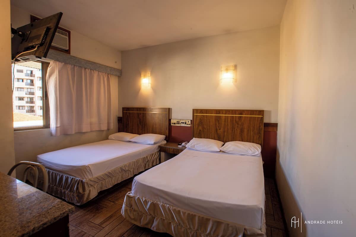 A hotel room with two single beds, a wooden headboard, a small desk, and a window with curtains.