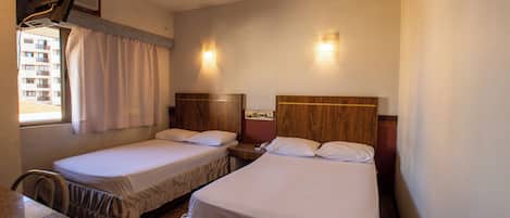 A hotel room with two single beds, a wooden headboard, a desk, and a window with curtains.