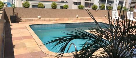 A rectangular pool with a tiled deck, surrounded by a low brick wall and potted plants.