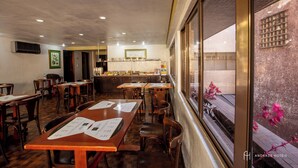 A restaurant with wooden tables and chairs, a kitchen area, and a view through a window. - Rede Andrade São Francisco (Curitiba)