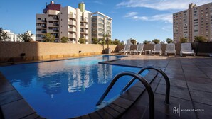 A swimming pool with a clear blue water, surrounded by lounge chairs and a brick wall. - Rede Andrade São Francisco (Curitiba)