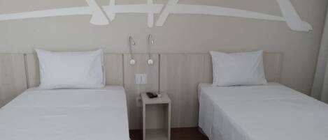 Habitación de hotel con dos camas individuales, una mesita de noche pequeña con lámpara, y un aplique de pared.