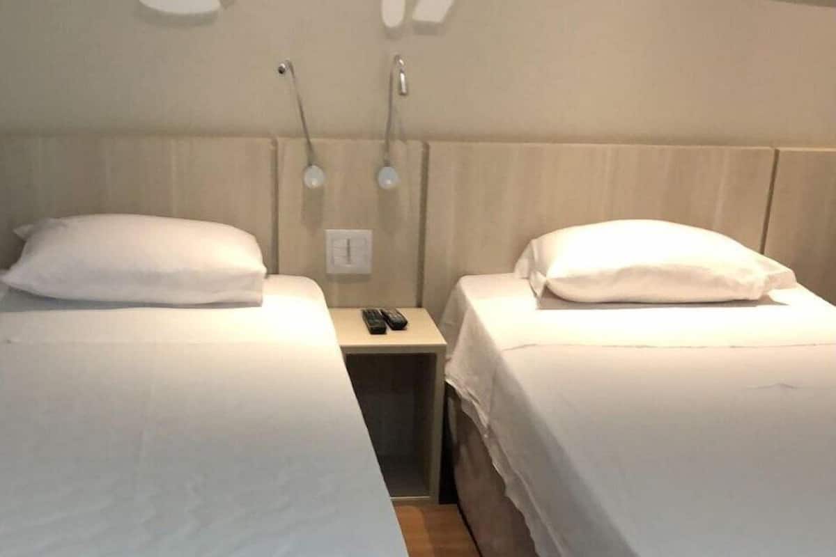 A hotel room with two single beds, wooden flooring, and a simple, clean design.