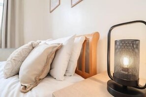 Una cama bien hecha con almohadas y una lámpara de escritorio negra con pantalla de malla.