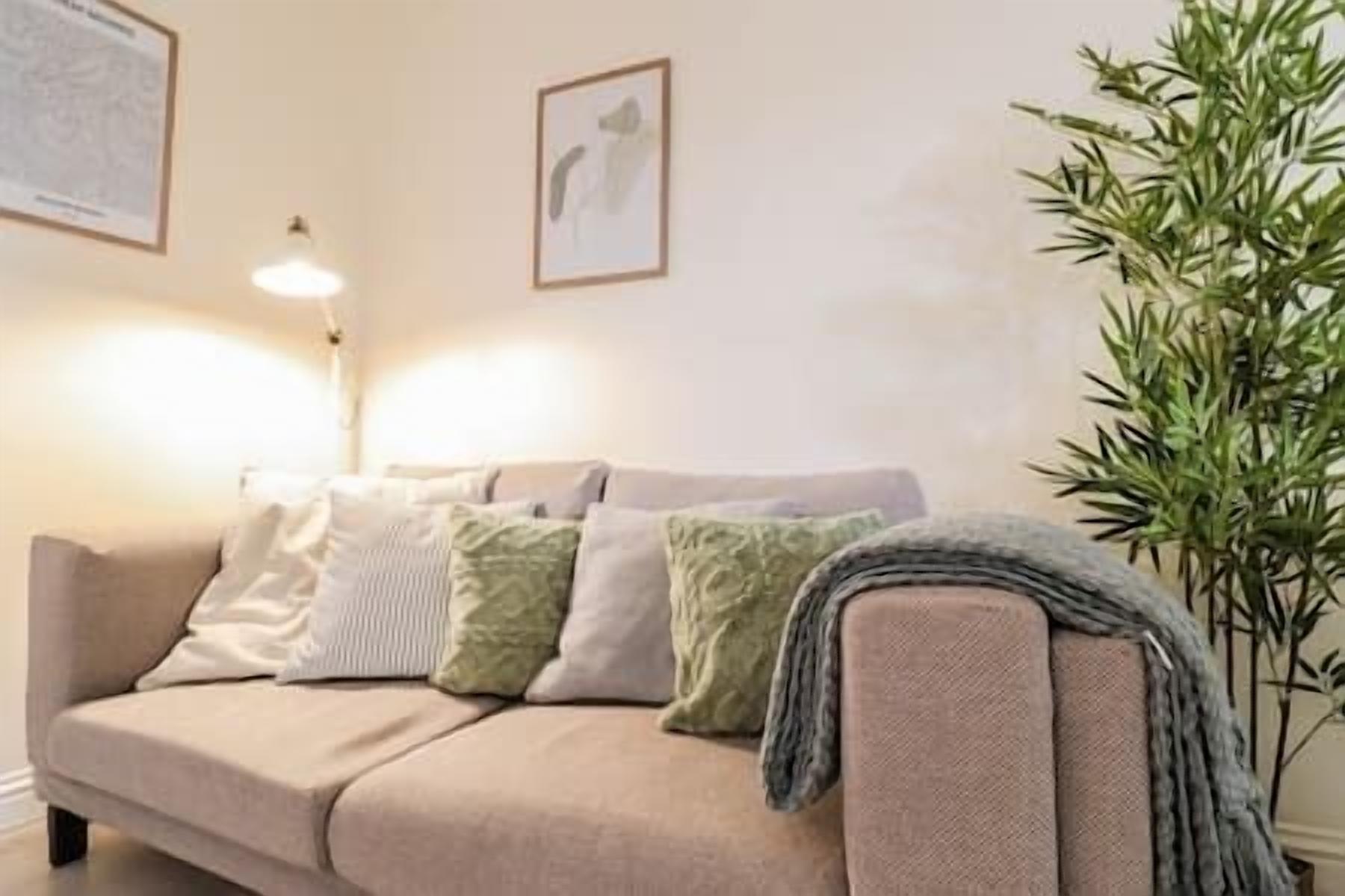 Ein beiges Sofa mit mehreren Kissen, einer Stehlampe und einem Blumentopf in einem Wohnzimmer.