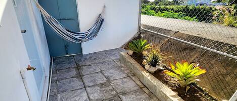 A small outdoor patio with stone tiles, a hammock, and a potted plant.