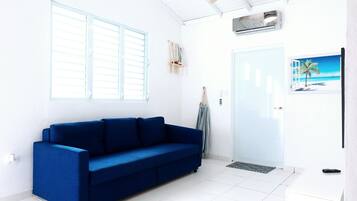 Ein helles Zimmer mit weißer Decke, einem blauen Sofa, einer Tür und einem an der Wand befestigten Fernseher.