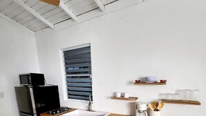 Une cuisine moderne avec des armoires blanches, un plan de travail en bois, un évier encastré, un four à micro-ondes, un réfrigérateur et une fenêtre avec des stores.