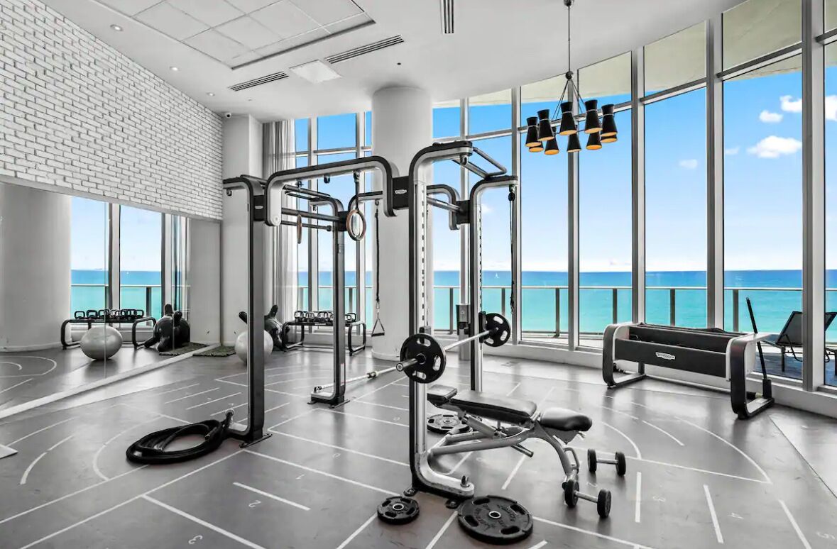 Une salle de sport équipée de matériel d’exercice, dotée de grandes fenêtres et offrant une vue sur l’océan.