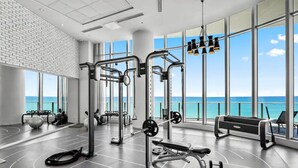 A gym with exercise equipment, large windows, and a view of the ocean.