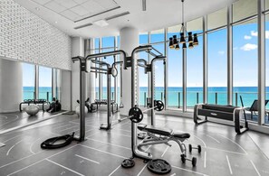 Une salle de sport équipée de matériel d’exercice, dotée de grandes fenêtres et offrant une vue sur l’océan.