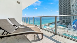 A balcony with two lounge chairs and a view of the ocean and a resort area.