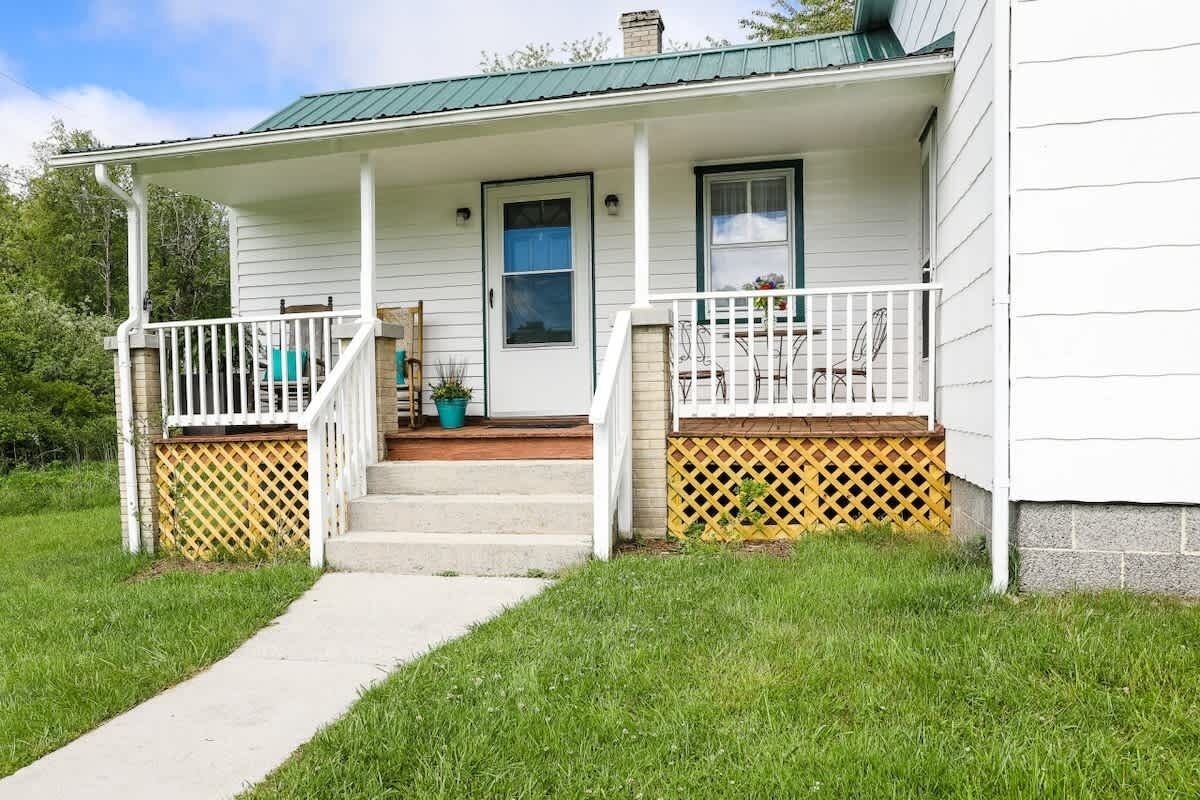 A white house with a porch, a front door, and a small set of steps leading to the entrance.