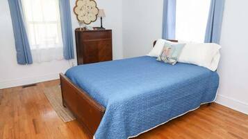 Quarto com cama de madeira, cômoda e janela com cortinas.