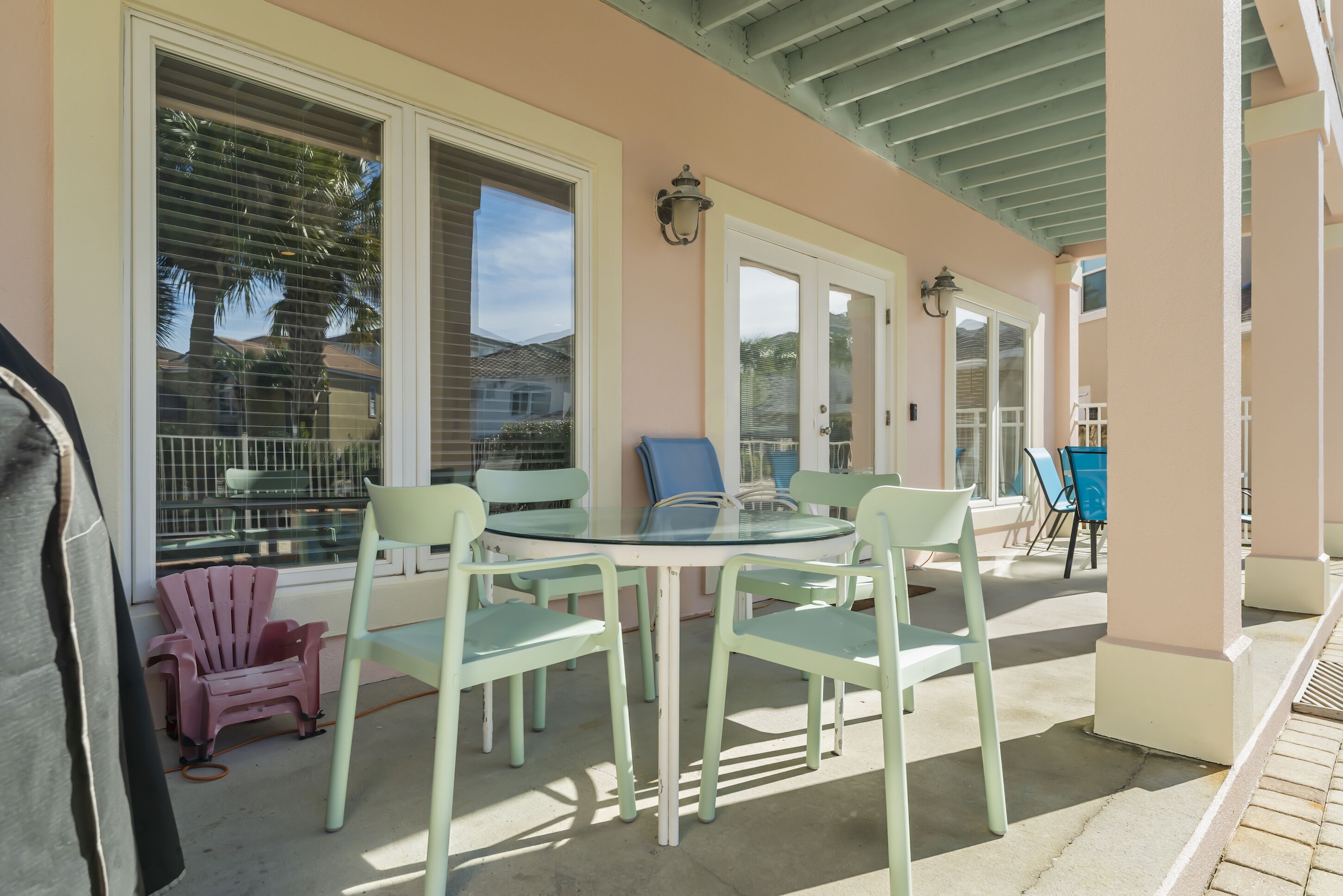 A covered patio with a round glass table and four chairs, a small pink chair, and a blue chair.