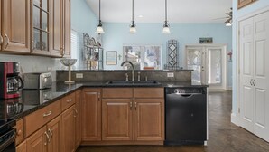 A kitchen with wooden cabinets, a black countertop, a dishwasher, and pendant lights. - Destin Beach House - Flamingo Cove (Miramar Beach)