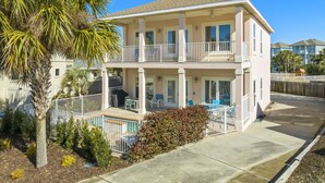 A two-story residential building with a balcony, a patio with outdoor furniture, and a pool area. - Destin Beach House - Flamingo Cove (Miramar Beach)