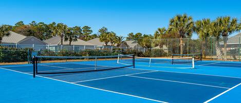 Una cancha de tenis con red, rodeada de palmeras y casas.