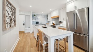 Une cuisine moderne avec des meubles blancs, un réfrigérateur en acier inoxydable et un îlot central doté de tabourets de bar.